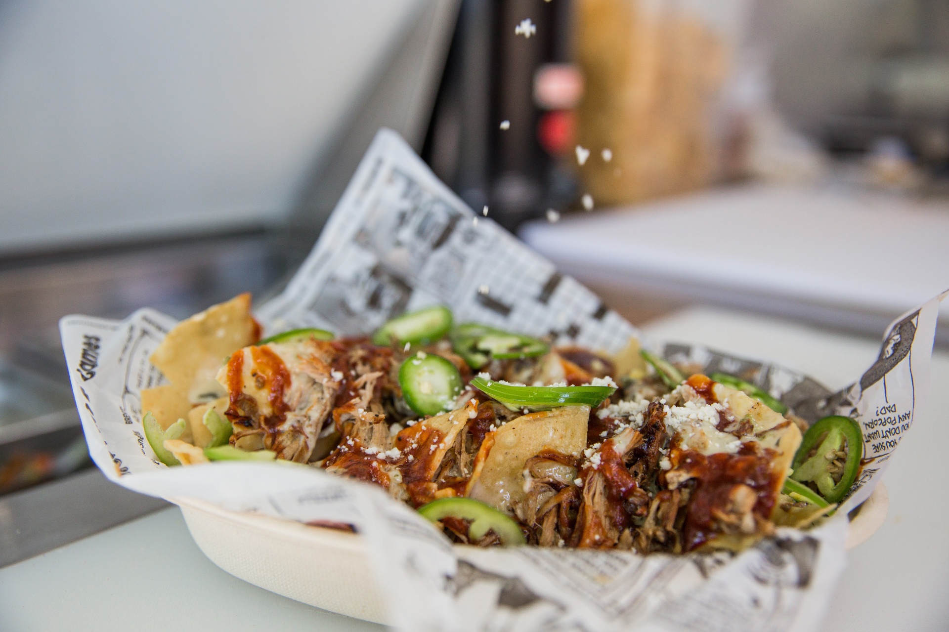 Cotija cheese sprinkled over pulled pork nachos in the truck window