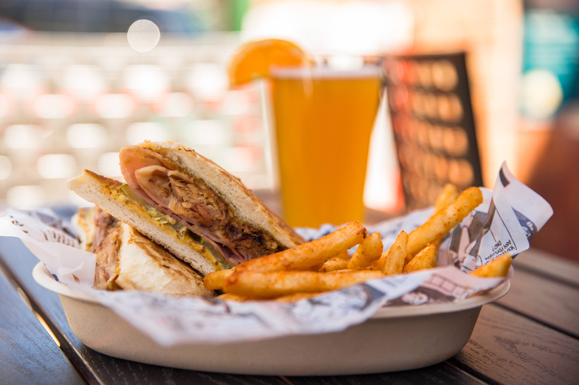 Cubano half stacked beside seasoned fries with a cold beer at golden hour